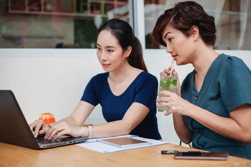 Two Asian women working together on a laptop in a café
