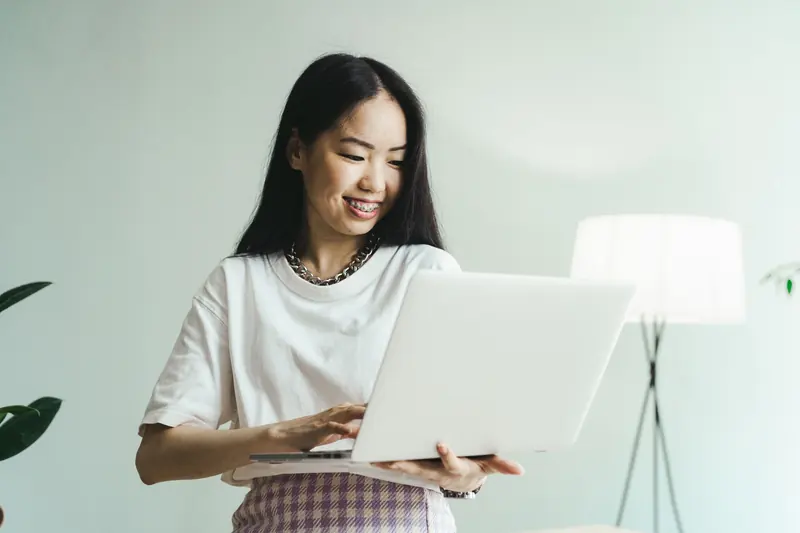 Smiling young Asian woman holding an open laptop at home
