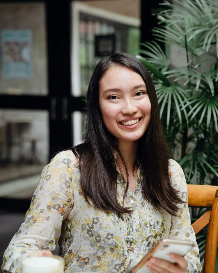 Young Asian woman smiling with her smartphone at a café table