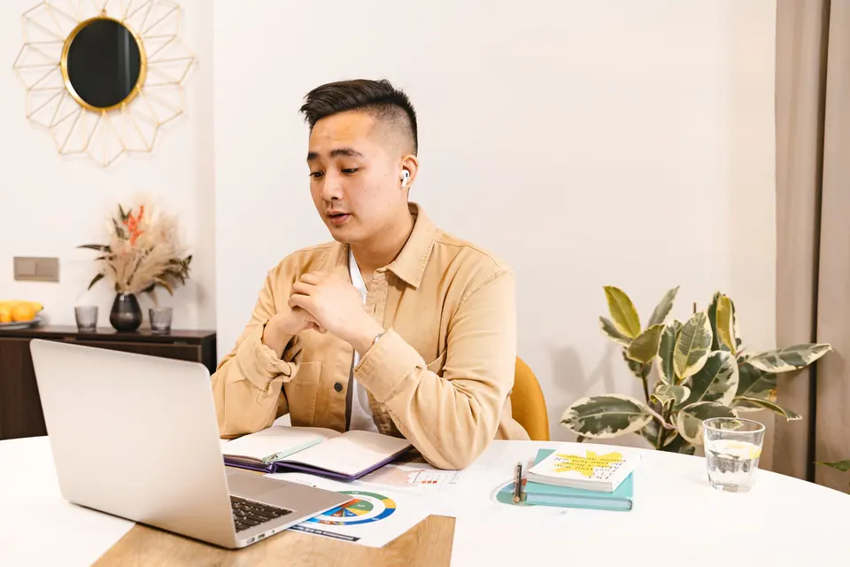 Asian professional reviewing notes beside his laptop at a modern desk